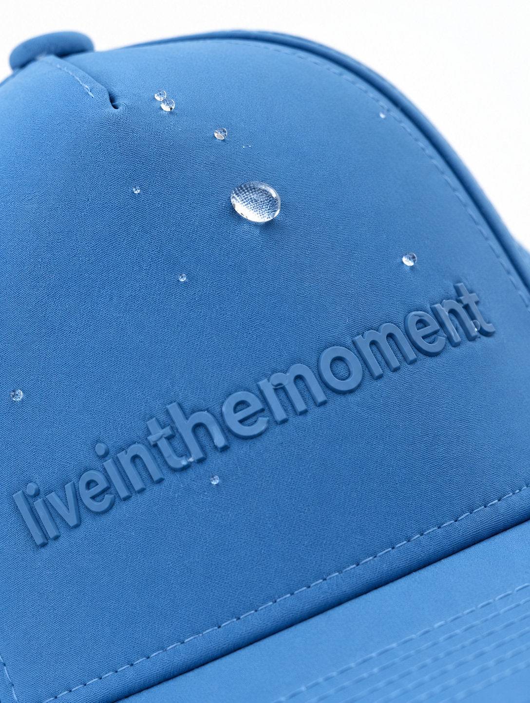 Water droplets beading on the blue MOJA Kids Live in the Moment cap, close-up of the raised lettering