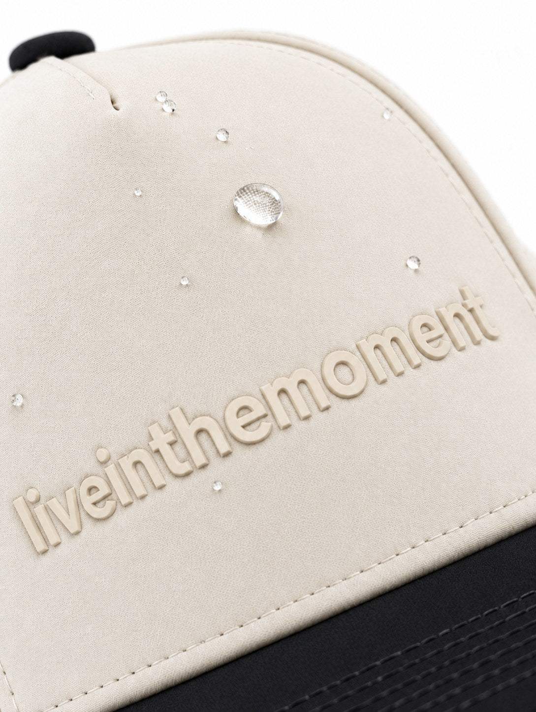 Water droplets beading on the ivory crown of the MOJA Kids Live in the Moment cap above the black brim